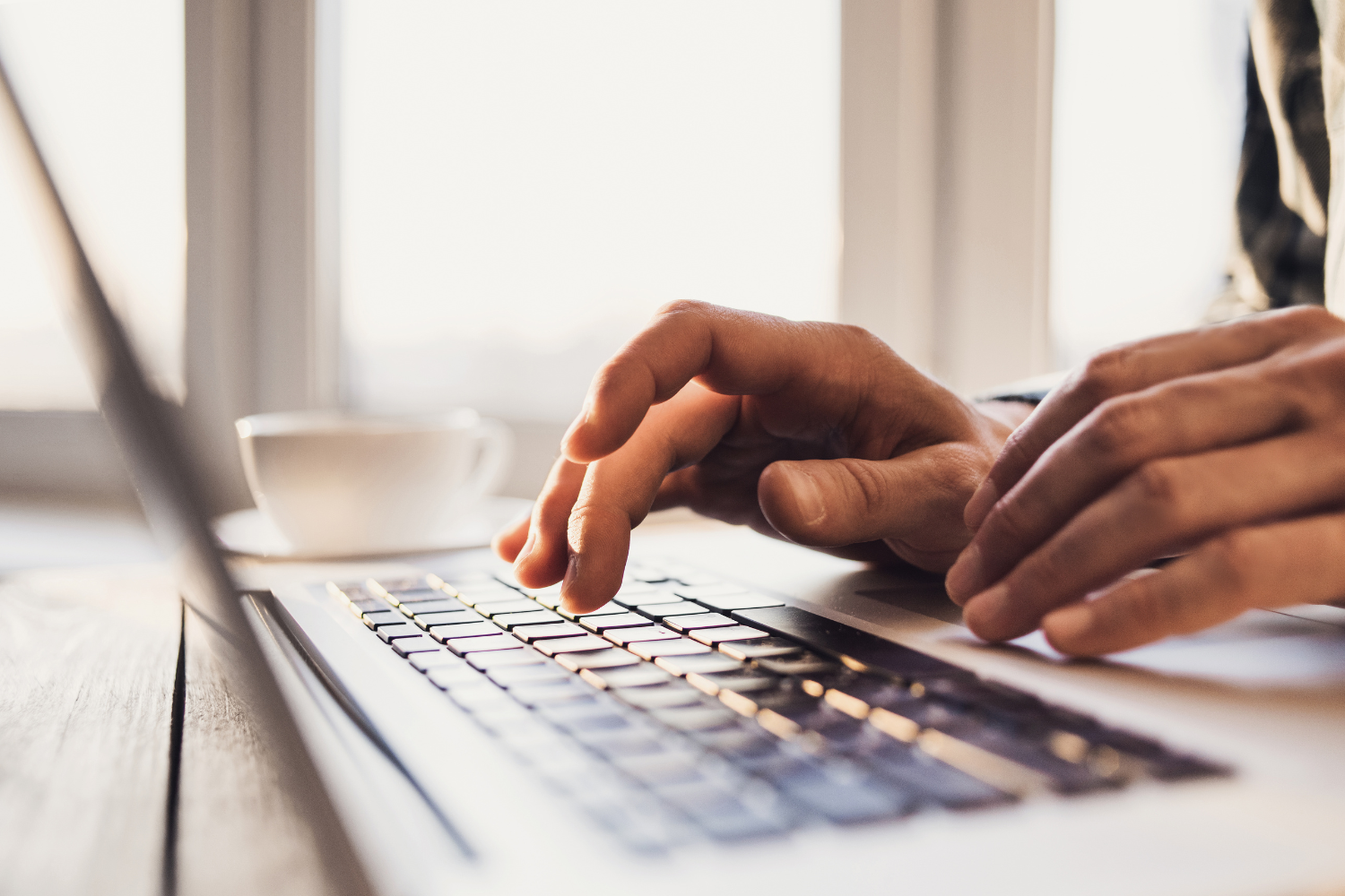 Hands typing on a laptop keyboard with an over exposed background